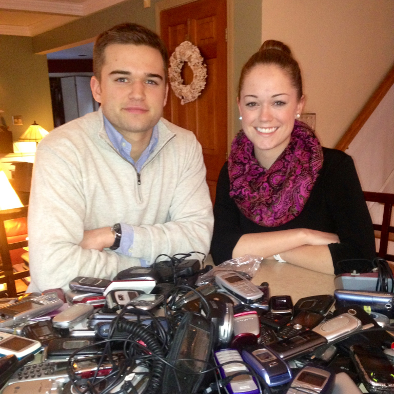 Brittany and Robbie Bergquist behind a large pile of assorted donated mobile phones on a table.