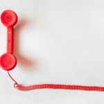 Red telephone handset with a coiled cord on a white background.